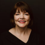 Headshot of Margaret Watkins, Ph.D., professor of philosophy, dean of the school of arts and sciences. Dr Watkins is smiling at the camera, wearing all black with red lipstick.