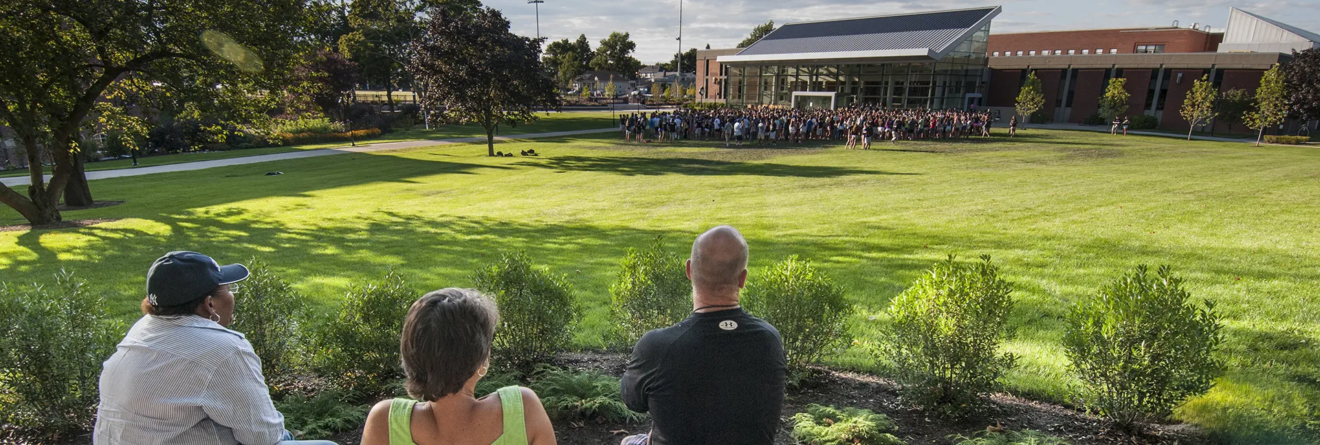 Three parents sit and watch their students participate in orientation activites on the Slavin lawn